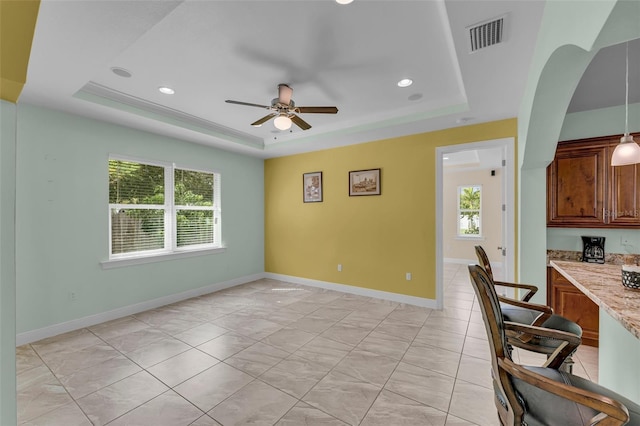 interior space with decorative light fixtures, a tray ceiling, light stone counters, and ceiling fan