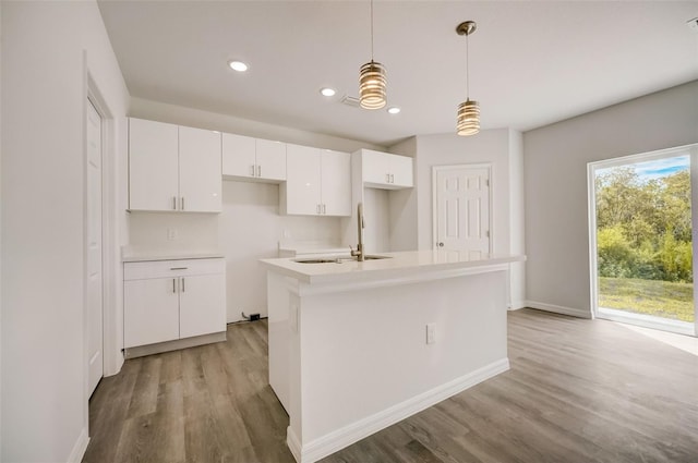 kitchen with light hardwood / wood-style flooring, a kitchen island with sink, decorative light fixtures, and white cabinetry