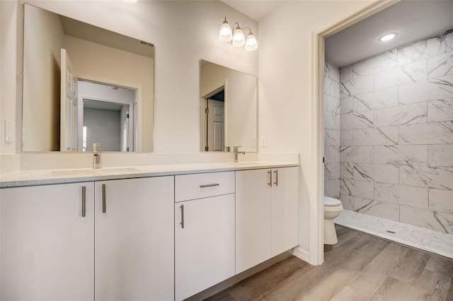 bathroom featuring wood-type flooring, a tile shower, vanity, and toilet