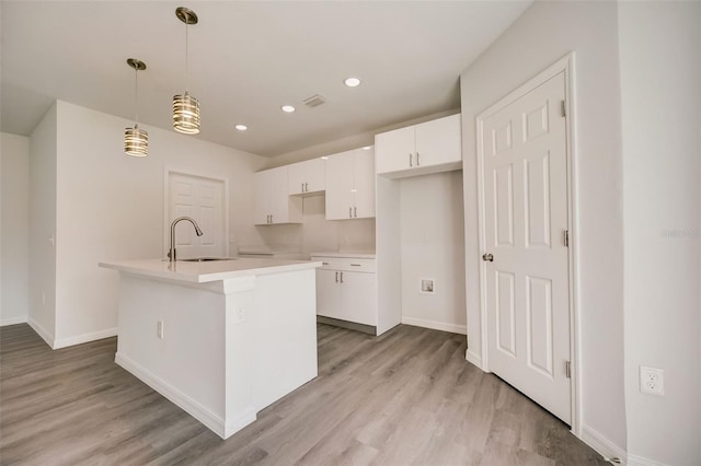 kitchen featuring white cabinets, pendant lighting, sink, a kitchen island with sink, and light hardwood / wood-style flooring