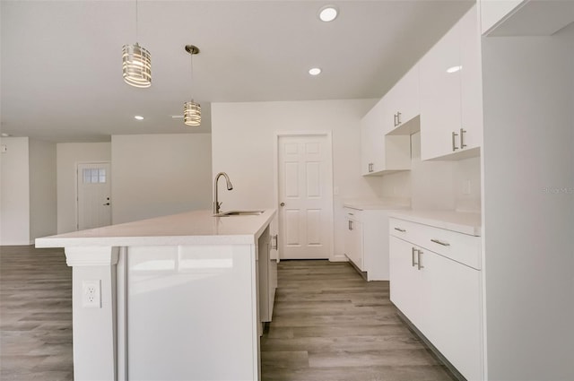 kitchen featuring white cabinets, sink, a center island with sink, decorative light fixtures, and hardwood / wood-style floors