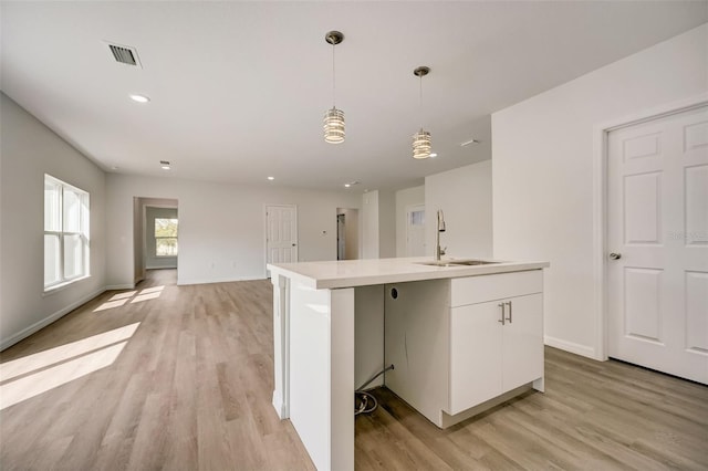 kitchen with light wood-type flooring, a kitchen island with sink, sink, and decorative light fixtures