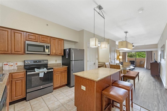 kitchen featuring light hardwood / wood-style floors, a center island, a breakfast bar area, stainless steel appliances, and light stone countertops