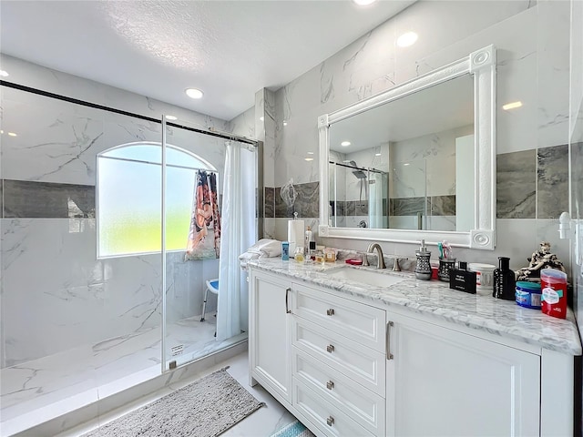 bathroom with a tile shower, vanity, and tile walls