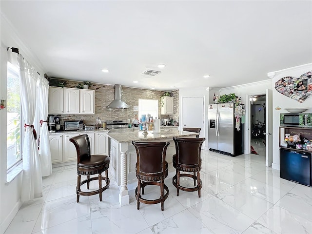 kitchen featuring appliances with stainless steel finishes, a center island, ornamental molding, wall chimney exhaust hood, and white cabinetry