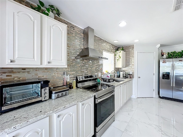 kitchen featuring light stone counters, wall chimney range hood, tasteful backsplash, white cabinetry, and appliances with stainless steel finishes