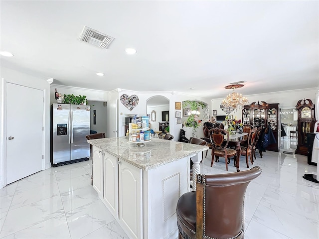 kitchen with crown molding, light stone counters, stainless steel refrigerator with ice dispenser, white cabinetry, and an inviting chandelier