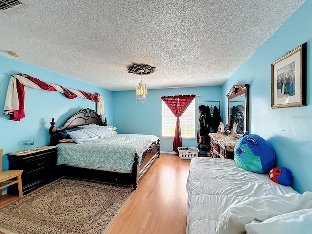 bedroom with wood-type flooring, an inviting chandelier, and a textured ceiling