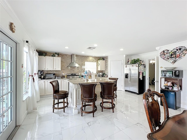 kitchen featuring stainless steel appliances, white cabinets, light stone counters, a kitchen island, and wall chimney range hood