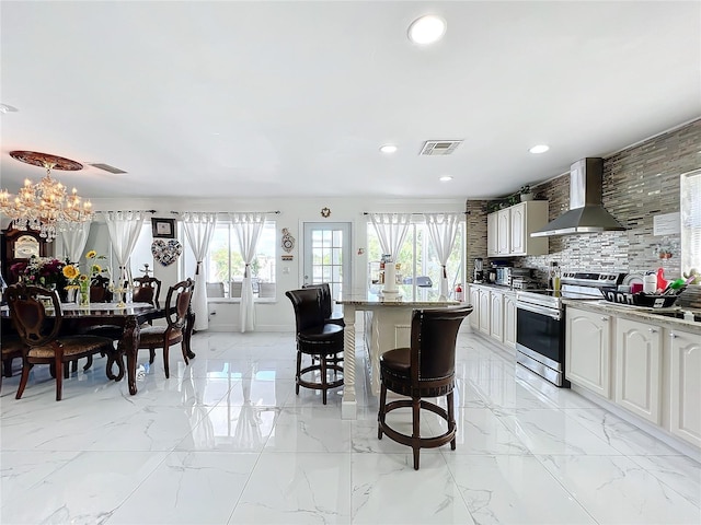 kitchen featuring an inviting chandelier, wall chimney exhaust hood, a kitchen breakfast bar, tasteful backsplash, and electric stove