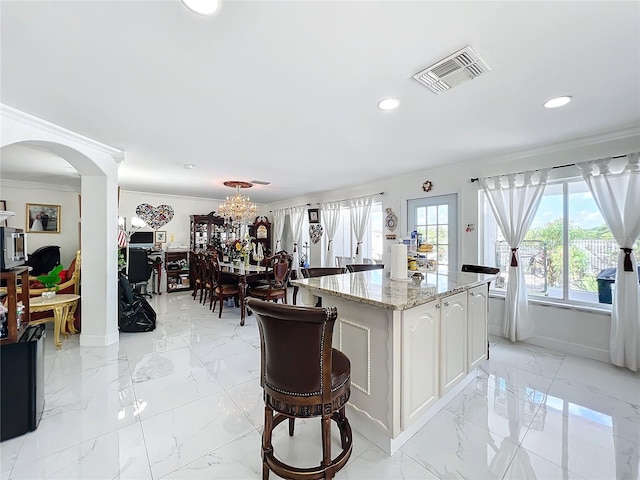 kitchen with light stone counters, a chandelier, a center island, white cabinets, and ornamental molding