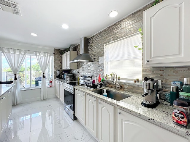 kitchen with stainless steel electric range, wall chimney exhaust hood, sink, white cabinetry, and backsplash