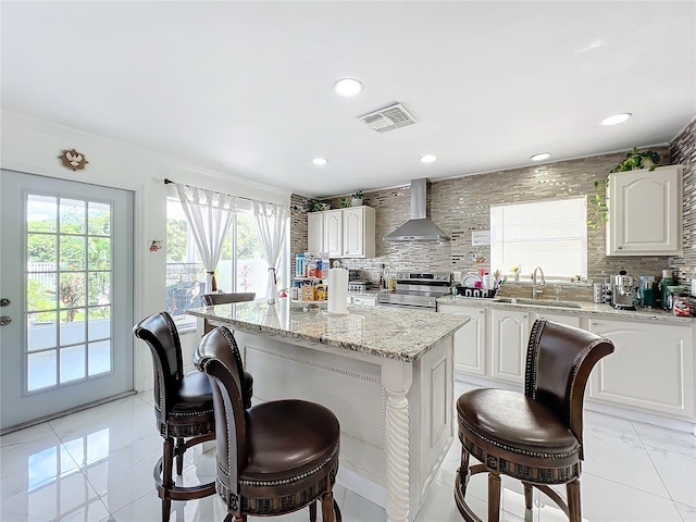 kitchen with sink, white cabinets, wall chimney exhaust hood, stainless steel electric range, and a kitchen island