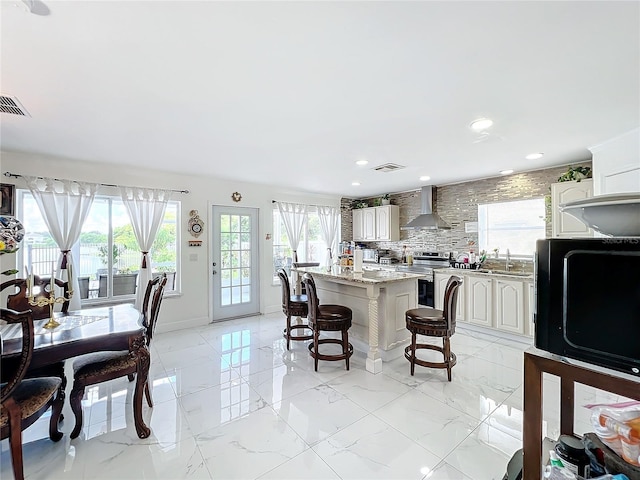 kitchen with light stone counters, wall chimney range hood, a kitchen bar, stainless steel electric range oven, and sink