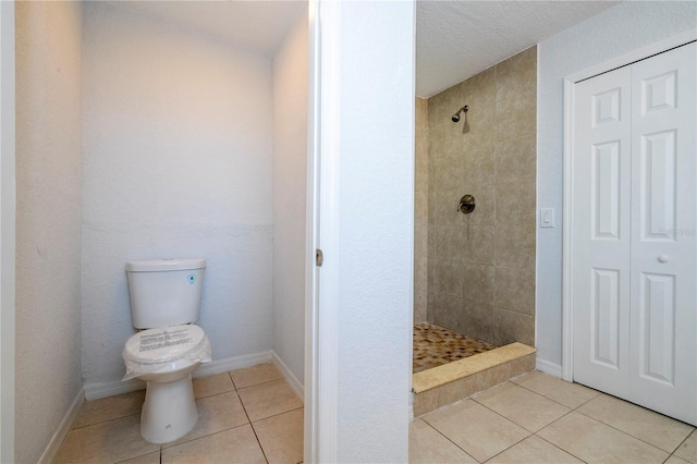 bathroom with toilet, a textured ceiling, tile patterned floors, and tiled shower