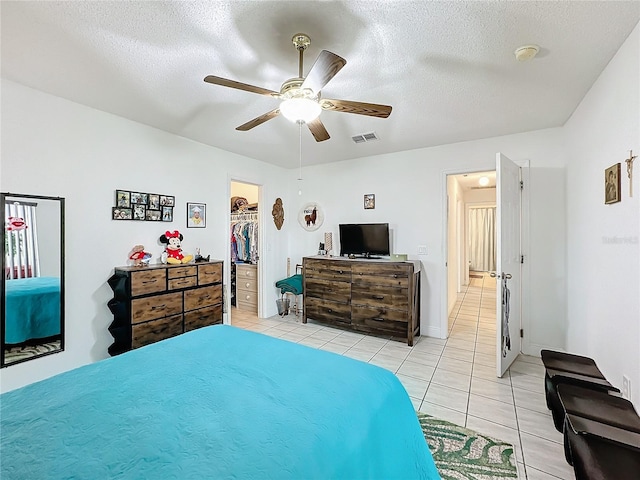 bedroom featuring ceiling fan, light tile patterned floors, a textured ceiling, a walk in closet, and a closet