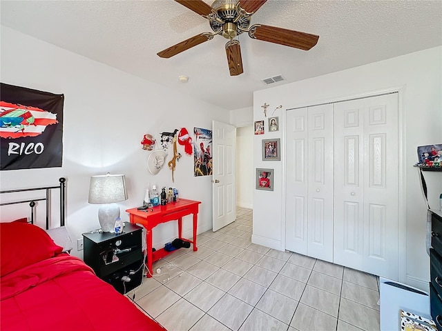 bedroom featuring a closet, ceiling fan, light tile patterned flooring, and a textured ceiling