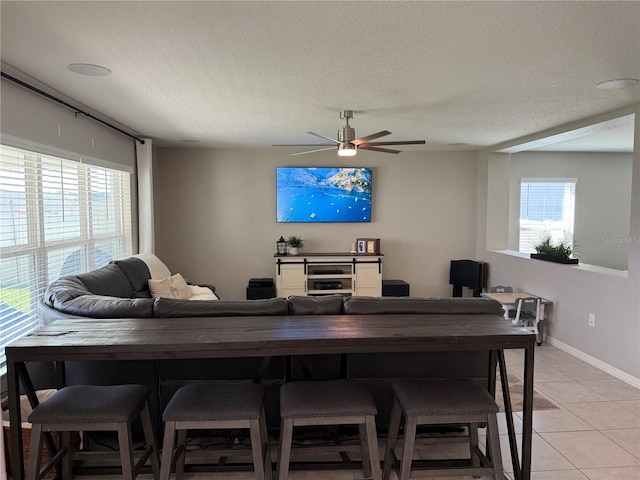 living room featuring a textured ceiling, light tile patterned floors, and ceiling fan