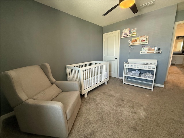 bedroom with a textured ceiling, a crib, carpet flooring, and ceiling fan