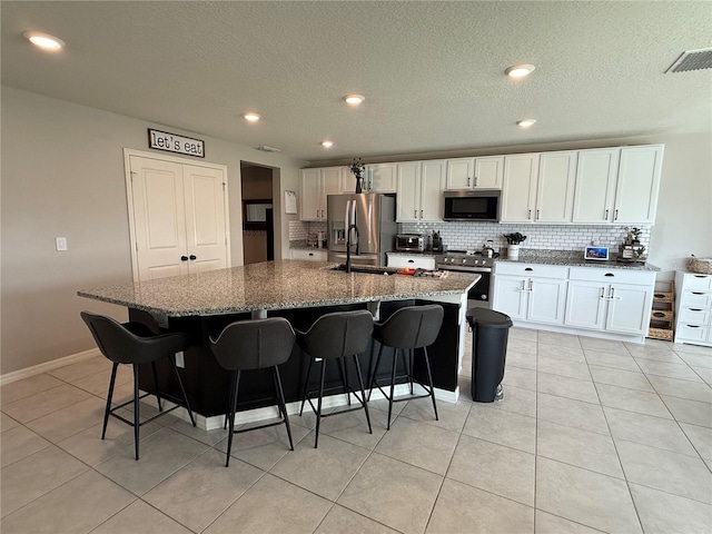 kitchen featuring stainless steel appliances, white cabinetry, a kitchen island with sink, and a breakfast bar