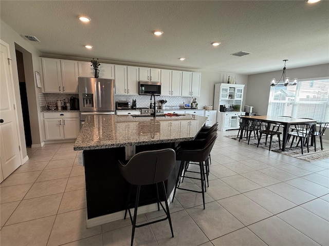 kitchen with white cabinets, appliances with stainless steel finishes, stone countertops, light tile patterned floors, and a center island with sink