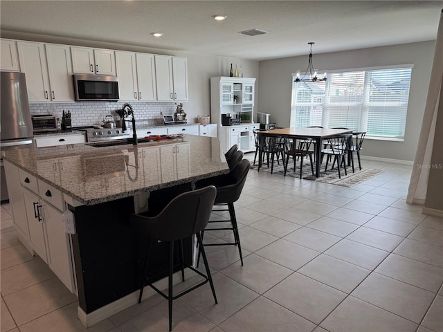 kitchen featuring white cabinets, an island with sink, dark stone countertops, and appliances with stainless steel finishes