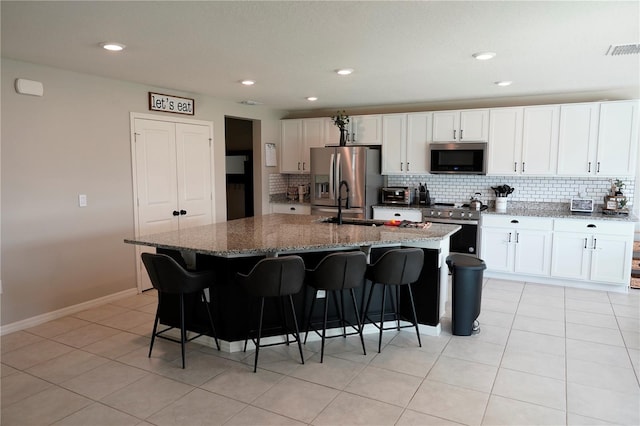 kitchen featuring a center island with sink, white cabinets, dark stone counters, and appliances with stainless steel finishes