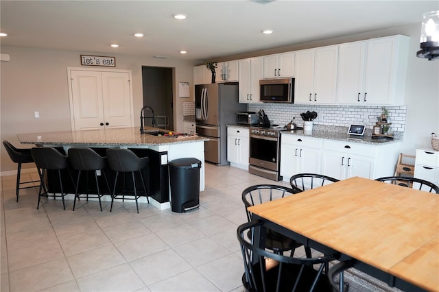 kitchen featuring light stone counters, white cabinets, a center island with sink, and stainless steel appliances