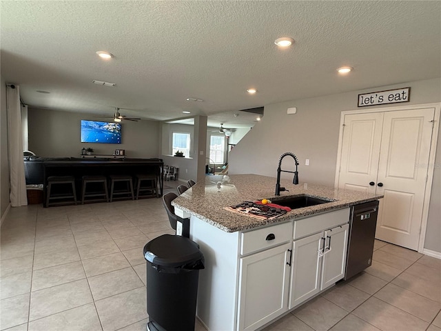 kitchen featuring dishwasher, sink, white cabinetry, an island with sink, and stone counters