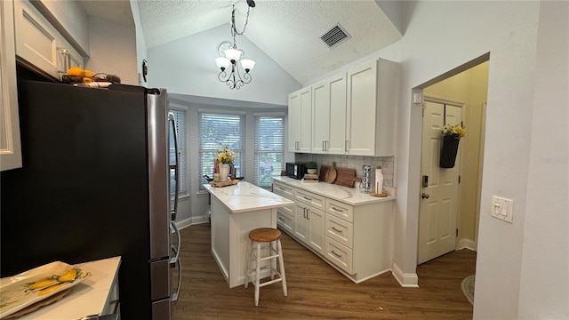 kitchen with white cabinets, stainless steel refrigerator, an inviting chandelier, a center island, and decorative light fixtures