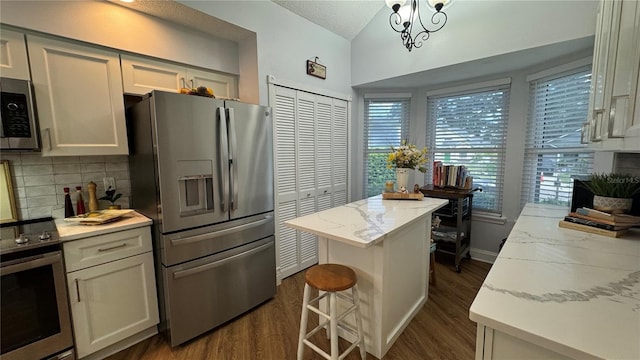 kitchen featuring appliances with stainless steel finishes, a kitchen island, light stone countertops, and dark wood-type flooring