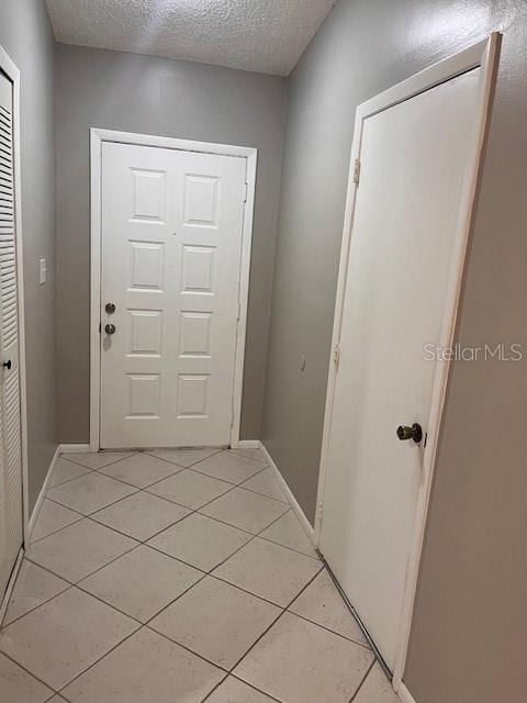 corridor featuring baseboards, a textured ceiling, and light tile patterned flooring