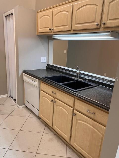 kitchen with dishwasher, light brown cabinets, dark stone countertops, sink, and light tile patterned flooring