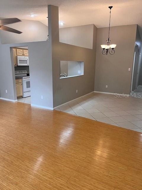 empty room with vaulted ceiling, light hardwood / wood-style flooring, and ceiling fan with notable chandelier