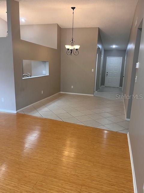 spare room with light hardwood / wood-style flooring, a chandelier, and vaulted ceiling