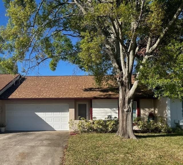 ranch-style home featuring a garage, roof with shingles, concrete driveway, and a front lawn