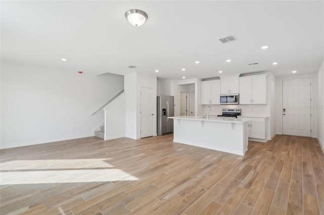 kitchen with stainless steel appliances, light wood-type flooring, a center island with sink, and white cabinets