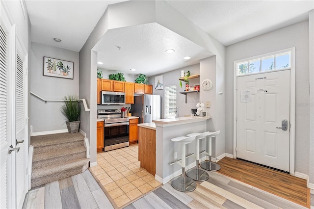 kitchen with appliances with stainless steel finishes, kitchen peninsula, light hardwood / wood-style flooring, and a kitchen bar