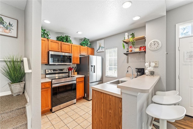 kitchen with a textured ceiling, sink, kitchen peninsula, a kitchen breakfast bar, and appliances with stainless steel finishes