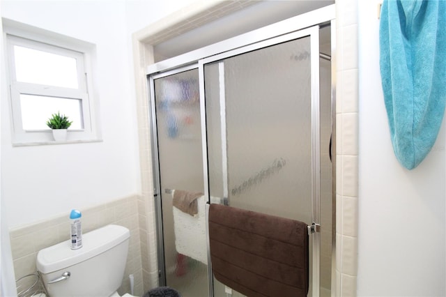 bathroom with tile walls, a shower with door, and toilet