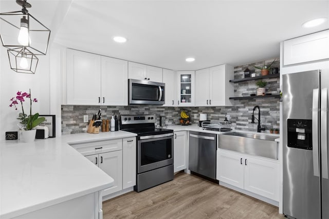 kitchen featuring stainless steel appliances, white cabinets, sink, hanging light fixtures, and light hardwood / wood-style flooring