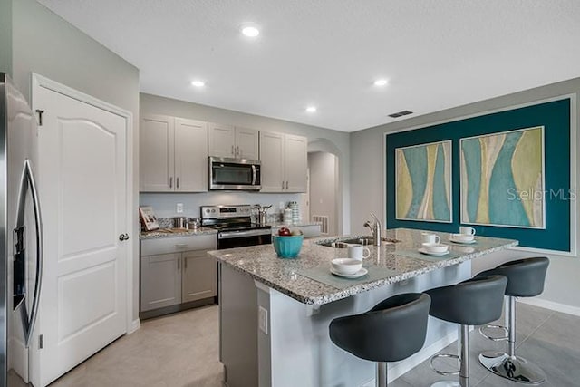 kitchen with a breakfast bar, sink, an island with sink, gray cabinetry, and stainless steel appliances