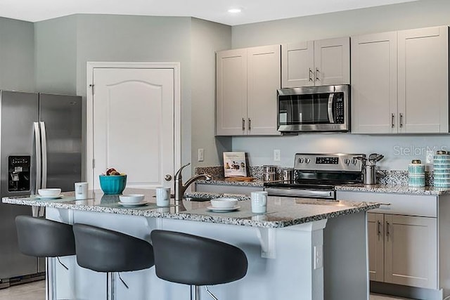 kitchen with an island with sink, light stone counters, and appliances with stainless steel finishes