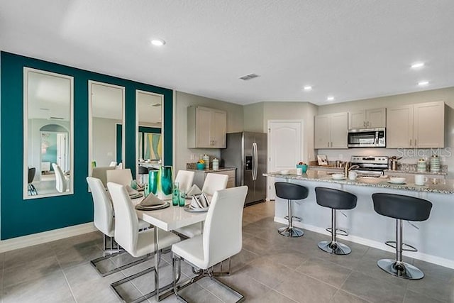 kitchen with light stone countertops, light tile patterned flooring, appliances with stainless steel finishes, and a kitchen breakfast bar