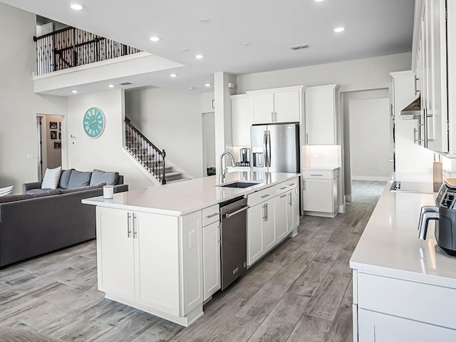 kitchen featuring sink, wall chimney range hood, a center island with sink, white cabinets, and appliances with stainless steel finishes