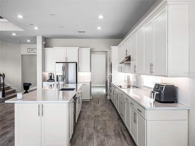 kitchen featuring white cabinetry, sink, stainless steel appliances, a large island with sink, and decorative backsplash