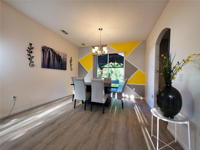 dining area featuring a textured ceiling, wood-type flooring, and a chandelier