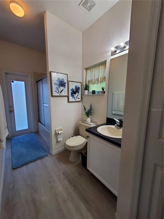 bathroom with hardwood / wood-style floors, a shower with shower door, vanity, and toilet