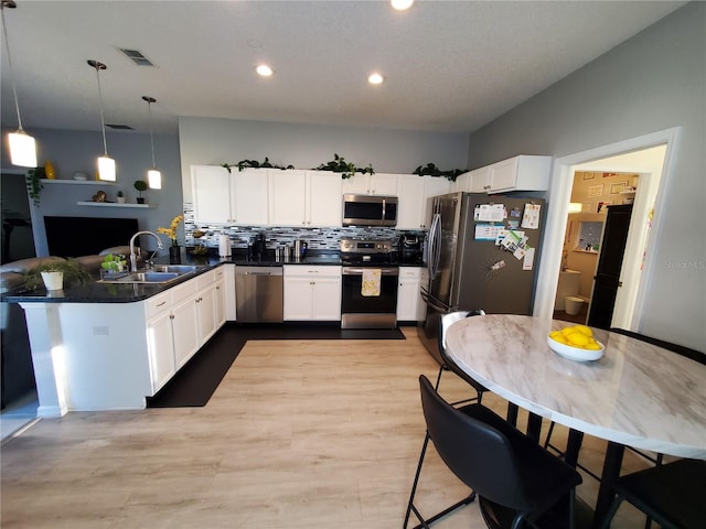 kitchen with appliances with stainless steel finishes, hanging light fixtures, white cabinetry, kitchen peninsula, and sink