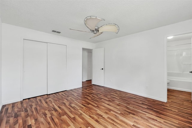 unfurnished bedroom with wood-type flooring, a closet, a textured ceiling, connected bathroom, and ceiling fan